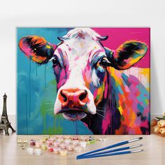 a painting of a cow with paintbrushes next to it on a wooden table