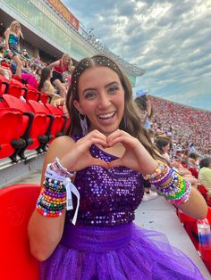 a woman in a purple dress is making a heart with her hands at a sporting event