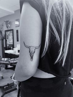 a woman's arm with a bull skull tattoo on the back of her left arm