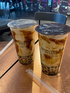 two iced coffees sitting on top of a table next to each other in plastic cups