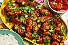 a platter filled with chicken wings and rice next to bowls of vegetables on a table