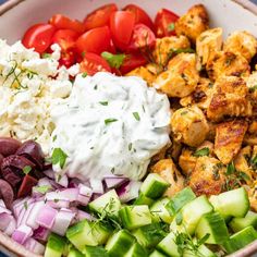 a bowl filled with chicken, cucumber, tomatoes, onions and other vegetables