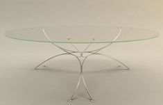 an oval glass table with metal legs on a plain surface, against a white background