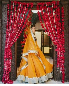 a woman in an orange and white lehenga is standing under red flower garlands