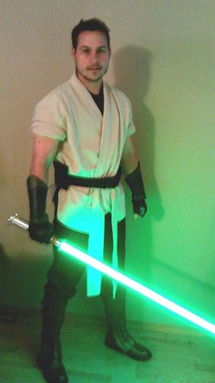 a man dressed as luke star wars holding a green light saber in his right hand