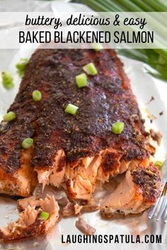 a piece of baked salmon on a plate with a fork and green onion garnish