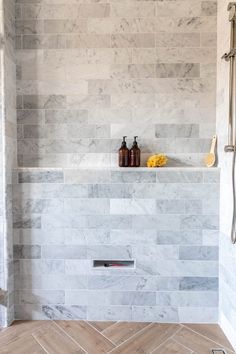 a bathroom with white marble tile and wooden flooring is shown in this image, there are two bottles on the shelf above the shower head