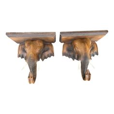 two wooden elephants head mounted to the back of a wall shelf, each with its trunk hanging down from it's sides