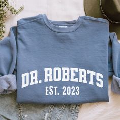 Looking for a unique and personal gift for a recent or soon-to-be PhD graduate? Look no further than this customizable PhD sweatshirt! Our sweatshirts are made from high-quality materials and come in a range of sizes to fit any body type. Plus, with the option to personalize the name on the sweatshirt, it's a one-of-a-kind gift that's sure to be treasured for years to come. To order, simply choose your preferred size and color, then enter the name you want to appear on the sweatshirt. We use only the highest-quality materials and printing techniques to ensure a long-lasting, vibrant print that won't fade or peel. This sweatshirt is perfect for anyone who's proud of their academic accomplishments and wants to show it off in style. Please take a moment to read carrefully the information prov Customizable Cotton T-shirt For College, Customizable Crew Neck Tops For College, Customizable Crew Neck T-shirt For School, Collegiate Customizable Crew Neck Tops, Phd Planning, Phd Party, Phd Shirt, Phd Graduate, Phd Humor