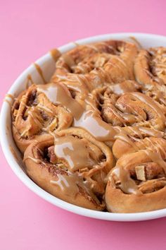 a bowl filled with cinnamon rolls covered in icing on top of a pink table