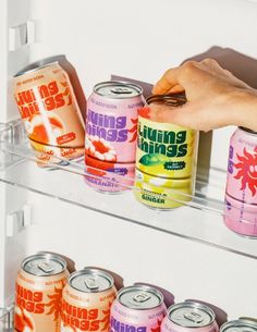 a person reaching for cans of soda on a shelf in a refrigerator with other drinks