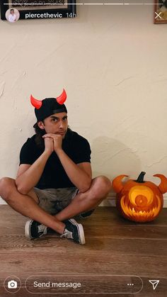 a man sitting on the floor with his hands under his chin and wearing devil horns