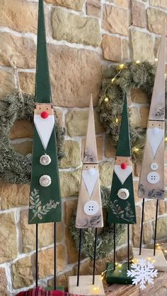 three wooden gnomes are on display in front of a brick wall with wreaths