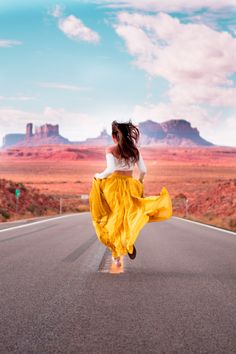 a woman is running down the road with her yellow dress in front of her and mountains in the background