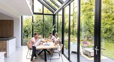 three people sitting at a table in the middle of a room with large glass walls