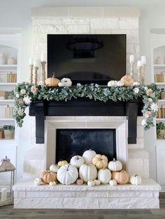 a fireplace decorated with white pumpkins and greenery