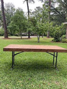 a wooden table sitting on top of a lush green grass covered park area with trees in the background