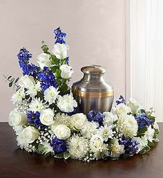 a vase with white and blue flowers sitting on a table next to a urn