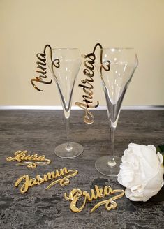 three wine glasses sitting on top of a table next to a white flower and some gold lettering