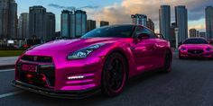 two pink sports cars driving down the road in front of tall buildings and skyscrapers