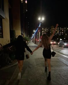 two women walking down the street at night with their hands in each other's pockets