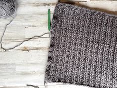 a gray and white knitted blanket next to a green crochet hook