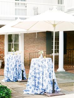 two tables with blue and white tablecloths are under an umbrella in front of a brick building