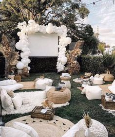 an outdoor movie party with white balloons and pillows on the grass in front of a large screen