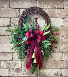 a christmas wreath hanging on the side of a brick wall with a red bow and bells