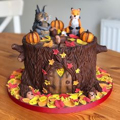 a cake decorated with animals and pumpkins on top of a wooden table in the shape of a tree stump