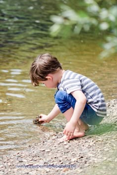 a young boy playing in the water with a rock at the river's edge