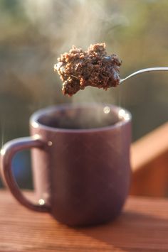 a spoon full of food sitting on top of a purple cup filled with liquid and steam