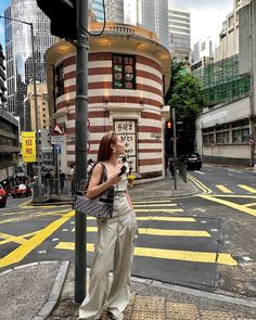 a woman standing on the side of a street next to a traffic light with buildings in the background