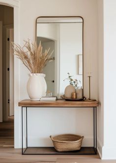 a white vase sitting on top of a wooden table next to a mirror and candle