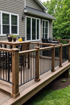 a wooden deck with black railings and chairs on the grass near a gray house