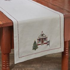 a table with a christmas tree on it and a house embroidered on the side,