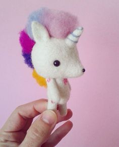 a hand holding a small stuffed animal with a rainbow mane on it's head