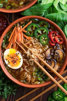 two bowls of ramen with chopsticks and an egg in the middle, surrounded by vegetables