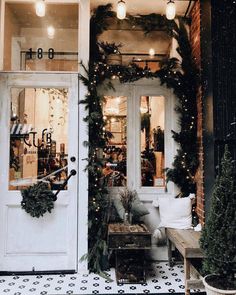 the front door of a store decorated with christmas wreaths and garlanded trees on either side