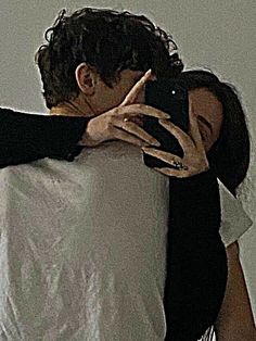 a man and woman embracing each other in front of a white wall