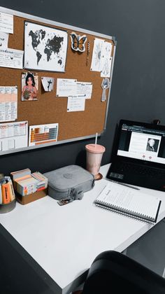 a laptop computer sitting on top of a white desk next to a cork board with notes