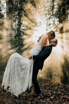 a bride and groom dancing in the woods at their outdoor wedding ceremony with sunbeams coming through the trees