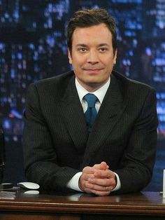 a man in a suit and tie sitting at a desk with his hands folded up