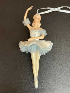 a ballerina ornament hanging from a string on a black table with a white ribbon