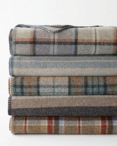 four plaid blankets stacked on top of each other in various colors and patterns, all folded neatly