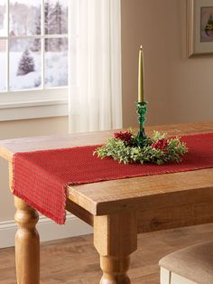 a wooden table topped with a candle and greenery on top of it next to a window