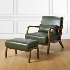 a green leather chair and footstool sitting on a hard wood floor in front of a white wall