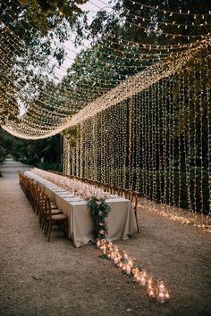 a long table with candles and lights on it in the middle of an outdoor area