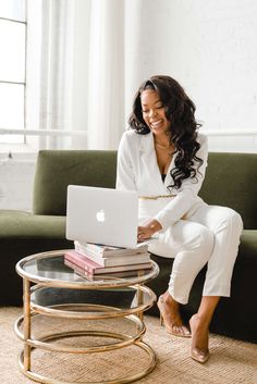 a woman sitting on a couch with a laptop in her lap and stack of books