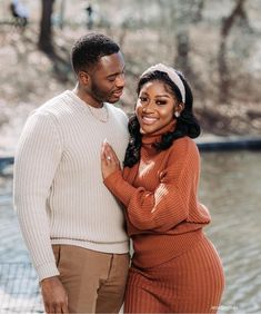 a man and woman standing next to each other in front of a body of water